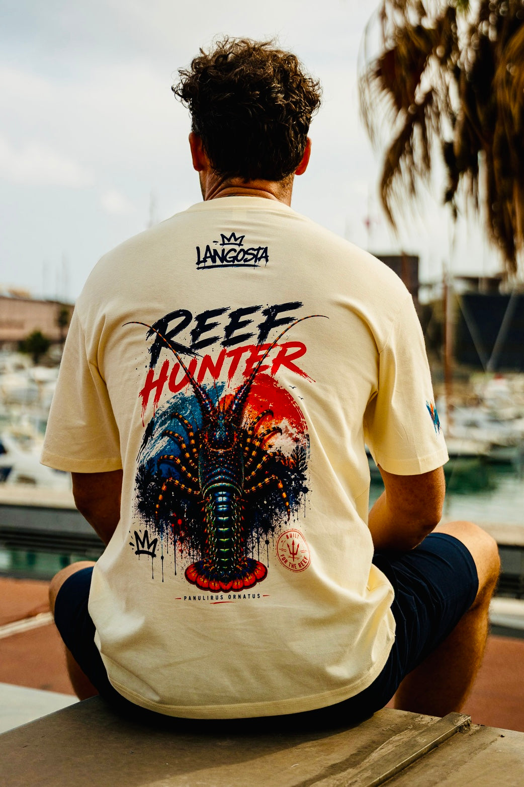 Modelo sentado vistiendo la camiseta Reef Hunter Fish on Replay con ilustración de langosta