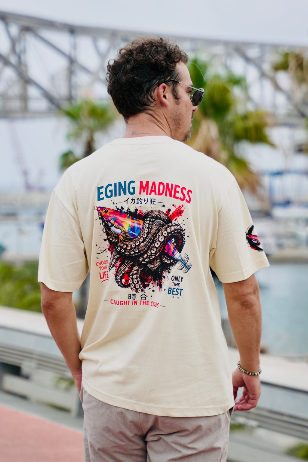 Modelo paseando y vistiendo la camiseta Eging Madness Fish on Replay en color beige 