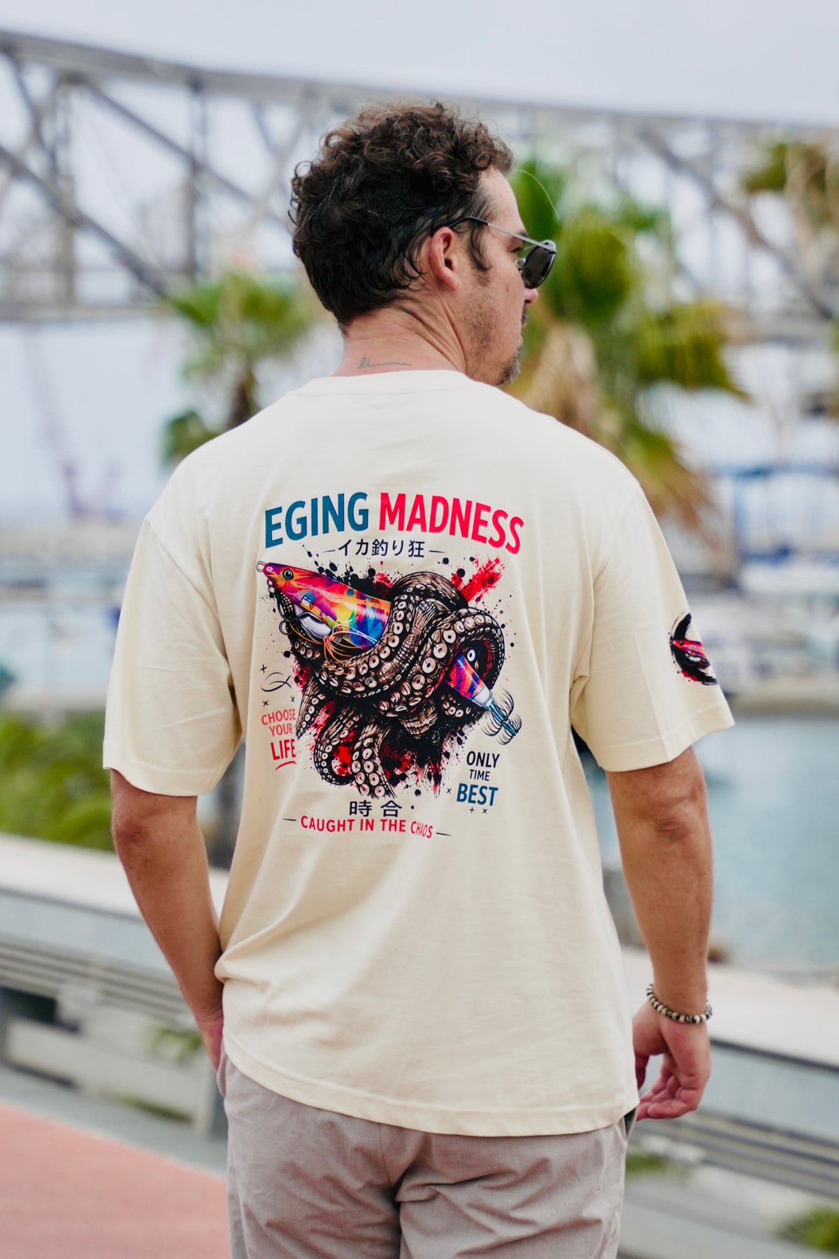 Modelo paseando y vistiendo la camiseta Eging Madness Fish on Replay en color beige 